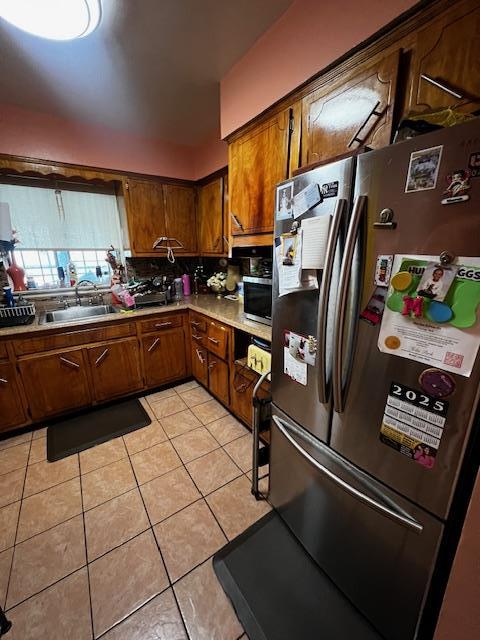 kitchen featuring light tile patterned flooring, a sink, freestanding refrigerator, and brown cabinets