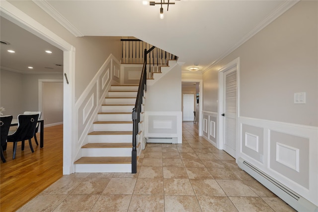 stairway featuring a wainscoted wall, a decorative wall, a baseboard radiator, and crown molding