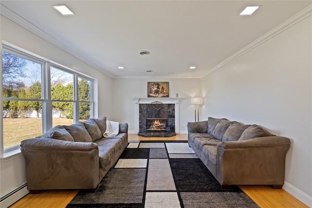 living room featuring a baseboard heating unit, ornamental molding, a tiled fireplace, and light wood-style flooring