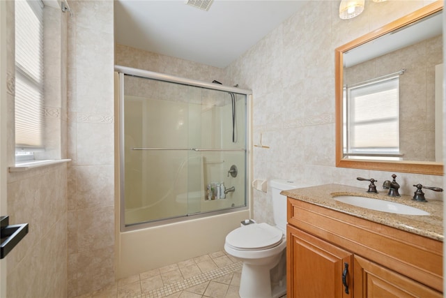 bathroom with tile walls, bath / shower combo with glass door, toilet, vanity, and tile patterned flooring