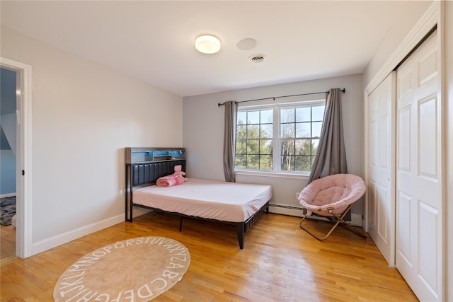 bedroom featuring baseboards, visible vents, baseboard heating, light wood-type flooring, and a closet