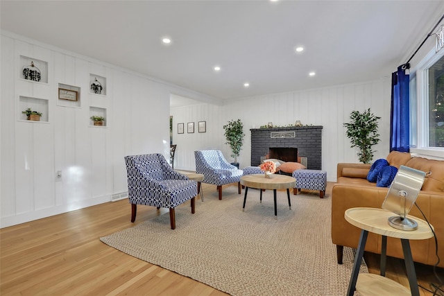 living area featuring a decorative wall, a brick fireplace, wood finished floors, and recessed lighting