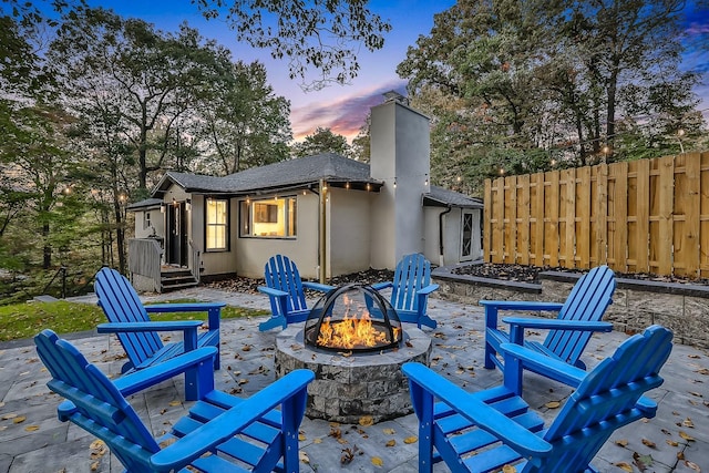 patio terrace at dusk featuring a fire pit and fence