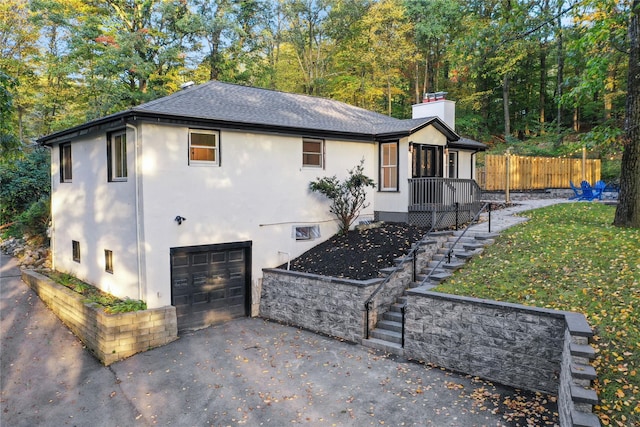 view of front facade featuring aphalt driveway, an attached garage, fence, stucco siding, and a chimney