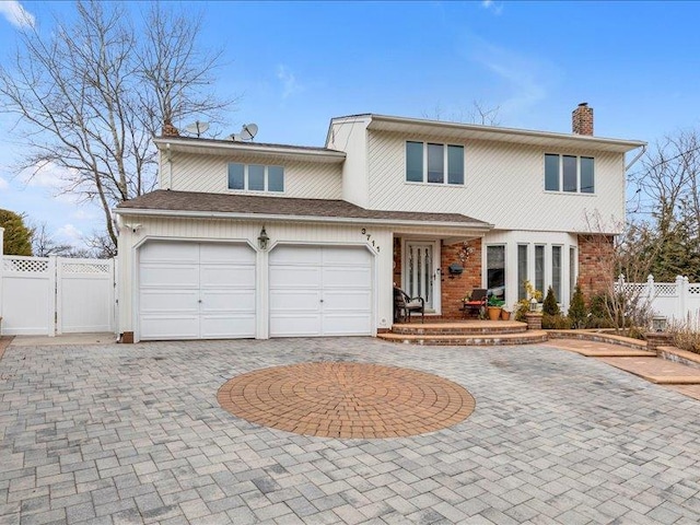 traditional-style home with brick siding, curved driveway, a chimney, a gate, and fence