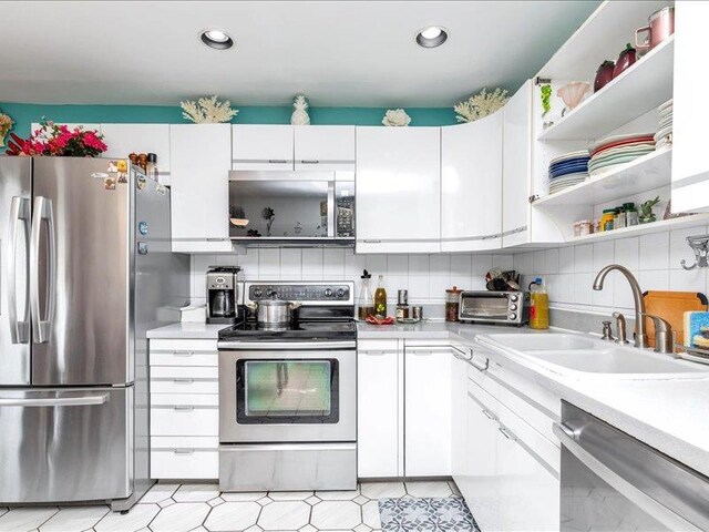 kitchen featuring white cabinets, appliances with stainless steel finishes, light countertops, open shelves, and a sink