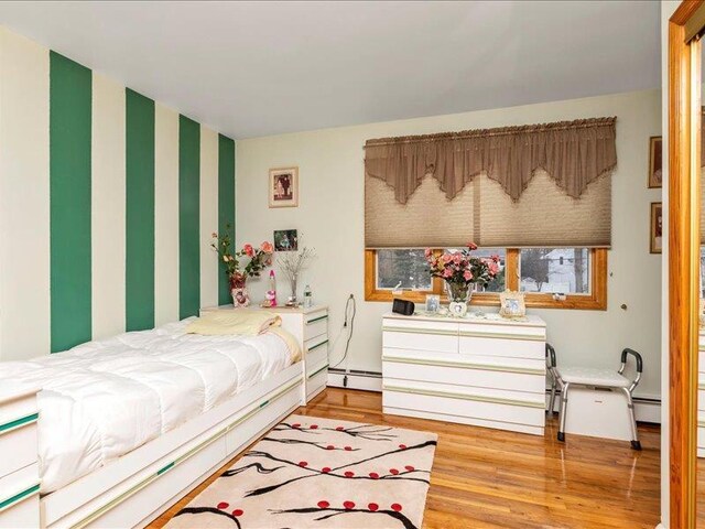 bedroom with a baseboard heating unit and wood finished floors