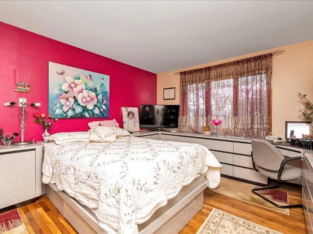 bedroom with an accent wall and wood finished floors