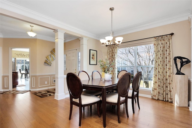 dining space with light wood-type flooring, decorative columns, ornamental molding, and a notable chandelier