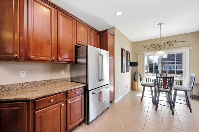 kitchen featuring baseboards, freestanding refrigerator, hanging light fixtures, light stone countertops, and light tile patterned flooring