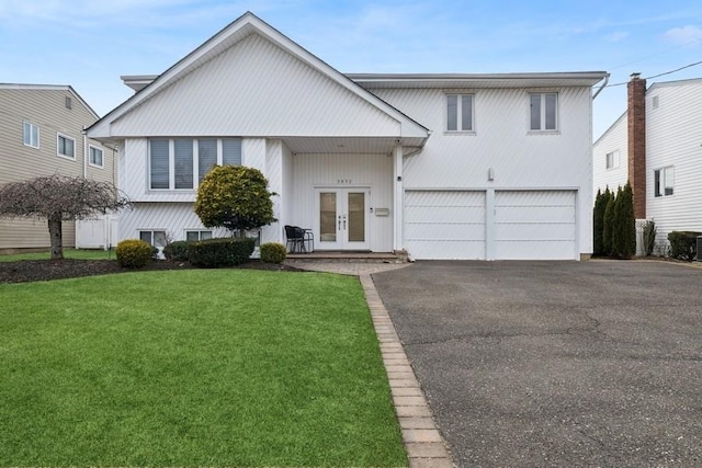 view of front of house featuring a front yard, an attached garage, french doors, and aphalt driveway