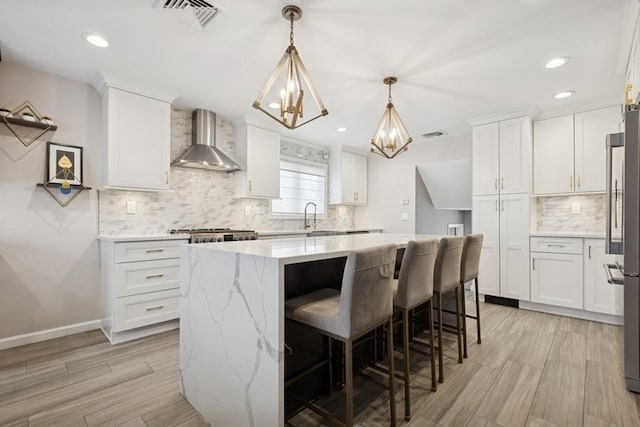 kitchen with visible vents, a kitchen island, freestanding refrigerator, white cabinetry, and wall chimney range hood