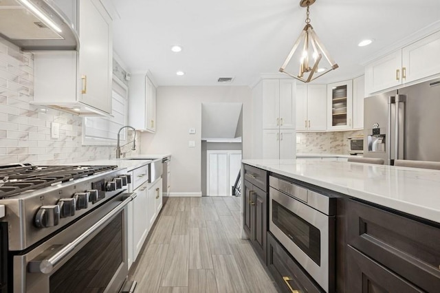 kitchen featuring white cabinets, ventilation hood, high end appliances, and an inviting chandelier