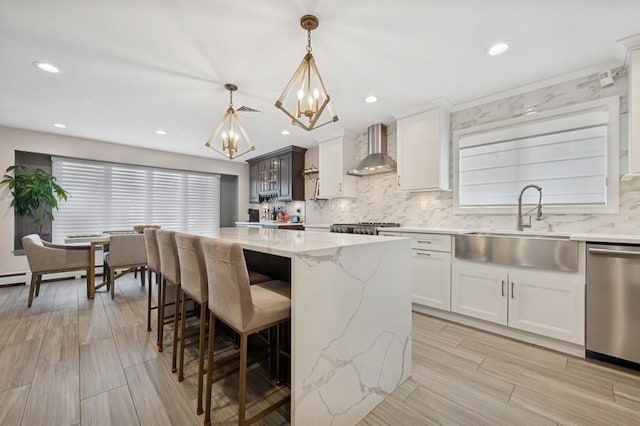 kitchen with a notable chandelier, a sink, a breakfast bar area, wall chimney range hood, and dishwasher