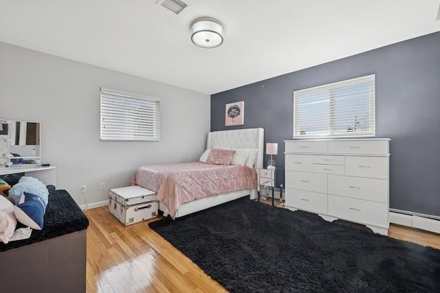 bedroom with baseboards, visible vents, a baseboard radiator, light wood-type flooring, and baseboard heating