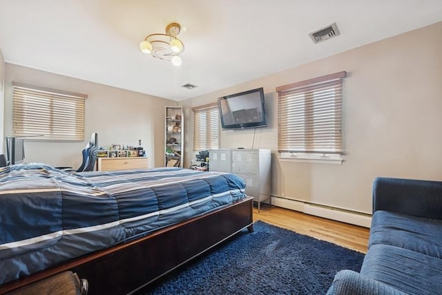 bedroom featuring visible vents, multiple windows, a baseboard heating unit, and wood finished floors