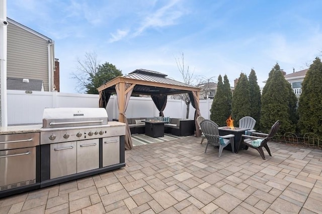 view of patio featuring exterior kitchen, a fenced backyard, an outdoor living space with a fire pit, a gazebo, and a grill