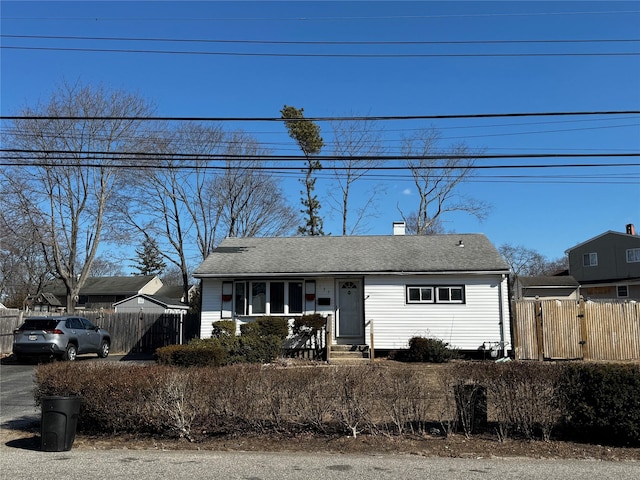 view of front of house featuring roof with shingles, fence, and a chimney