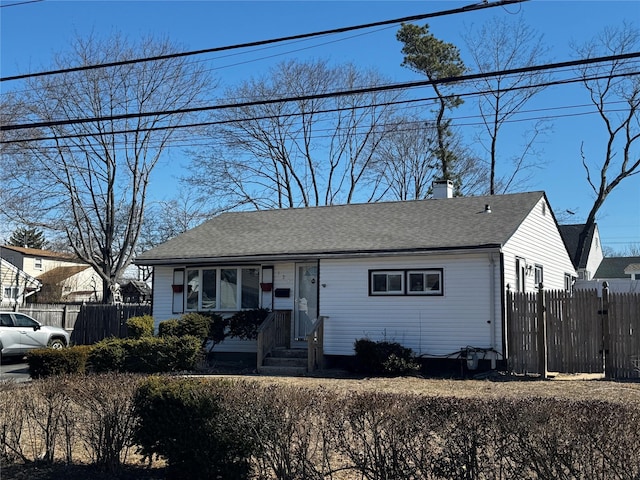 view of front of property with a shingled roof, a chimney, and fence