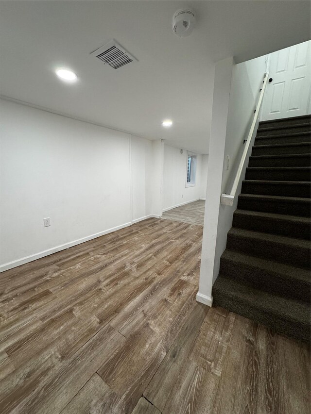 finished below grade area featuring stairway, baseboards, visible vents, and wood finished floors