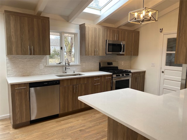 kitchen with appliances with stainless steel finishes, light countertops, a sink, and light wood finished floors