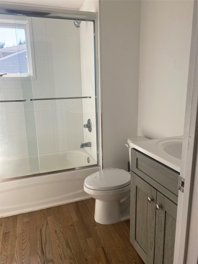 full bath with bath / shower combo with glass door, vanity, toilet, and wood finished floors