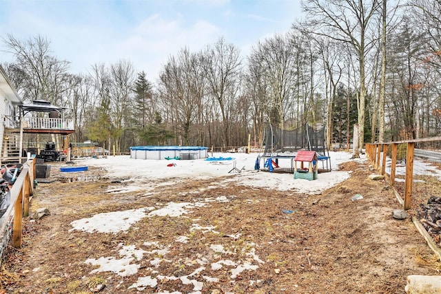 view of yard featuring a deck, a trampoline, fence, and an outdoor pool