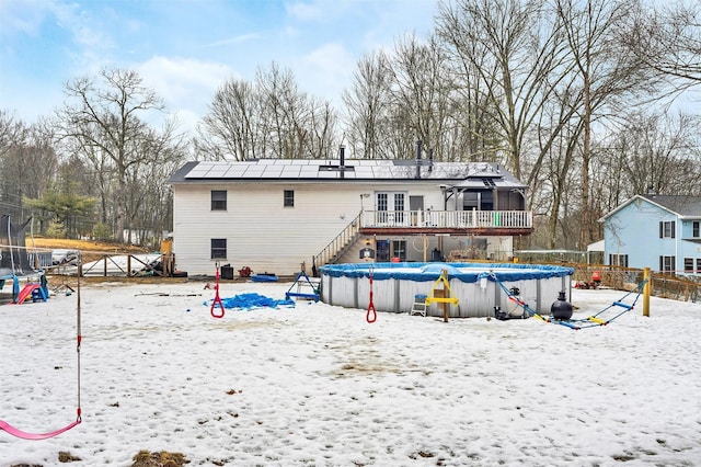 snow covered property featuring a trampoline, solar panels, fence, a covered pool, and a wooden deck