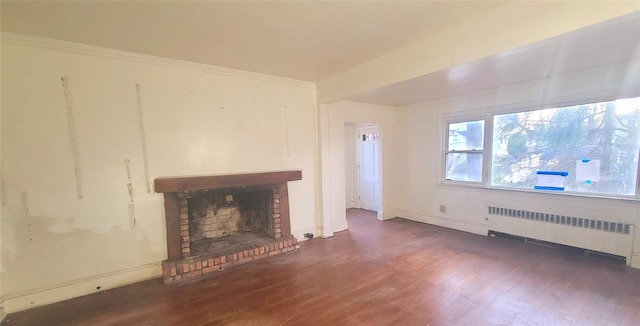 unfurnished living room featuring baseboards, radiator, wood finished floors, crown molding, and a brick fireplace