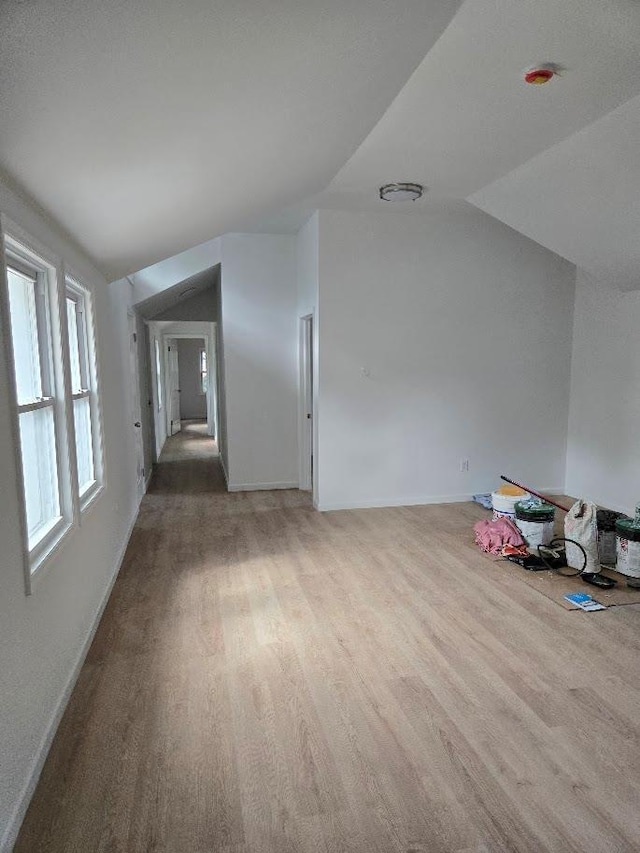 interior space with light wood-type flooring, baseboards, and vaulted ceiling