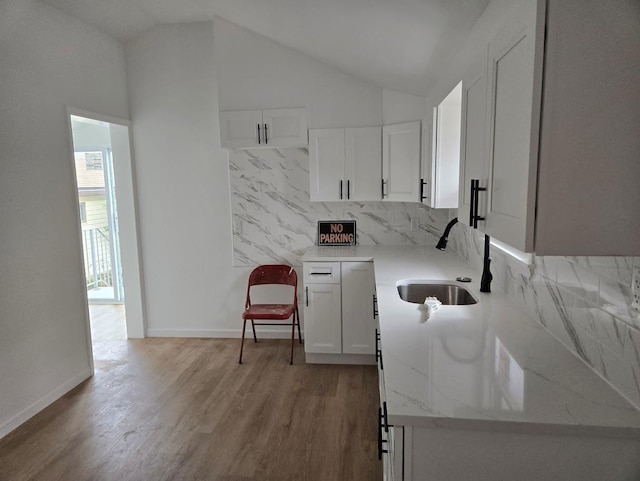 kitchen with lofted ceiling, light wood finished floors, a sink, and white cabinetry