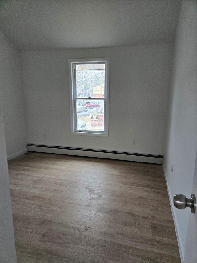 empty room featuring a baseboard heating unit, baseboards, and wood finished floors