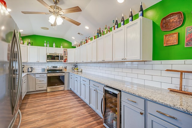 kitchen with lofted ceiling, wine cooler, light wood-style floors, appliances with stainless steel finishes, and backsplash