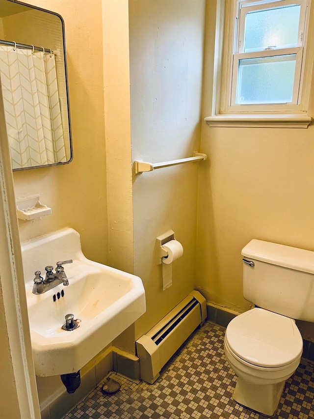 bathroom with baseboards, toilet, curtained shower, a baseboard heating unit, and a sink