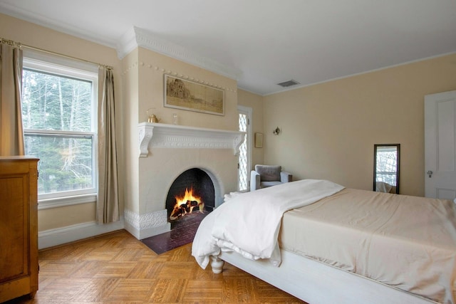 bedroom with a lit fireplace, baseboards, ornamental molding, and visible vents