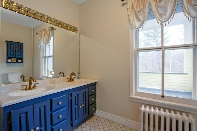 bathroom with radiator heating unit, double vanity, baseboards, and a sink