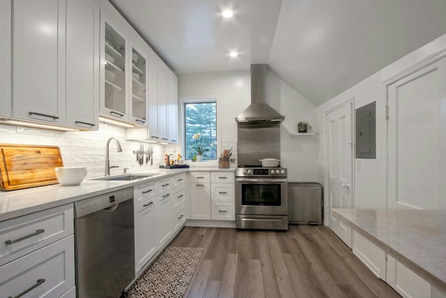 kitchen featuring electric panel, light wood-style floors, wall chimney exhaust hood, stainless steel appliances, and a sink