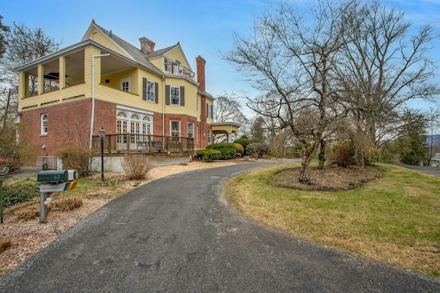 view of side of home with a balcony, a chimney, aphalt driveway, brick siding, and a yard