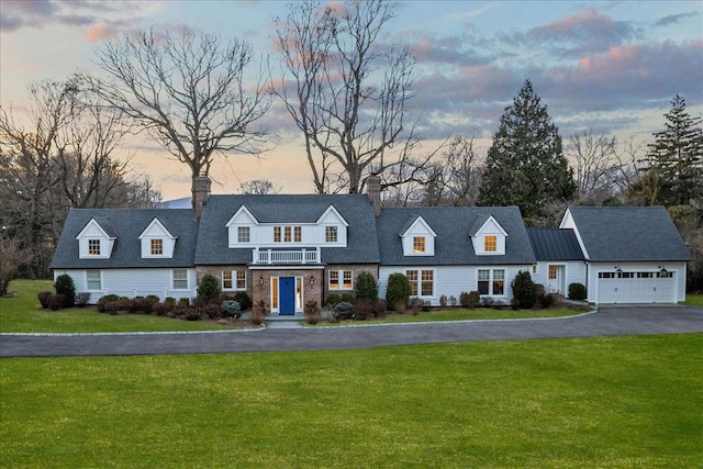 new england style home featuring aphalt driveway, an attached garage, and a front lawn