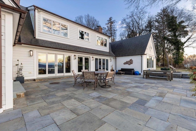 rear view of house featuring a patio, french doors, a chimney, and a shingled roof