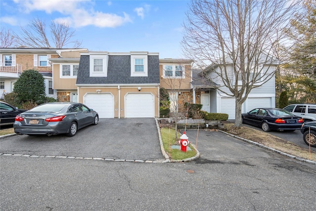 multi unit property with driveway, a shingled roof, a garage, and mansard roof