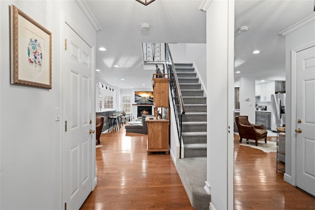 entryway featuring wood-type flooring, crown molding, a lit fireplace, and stairs