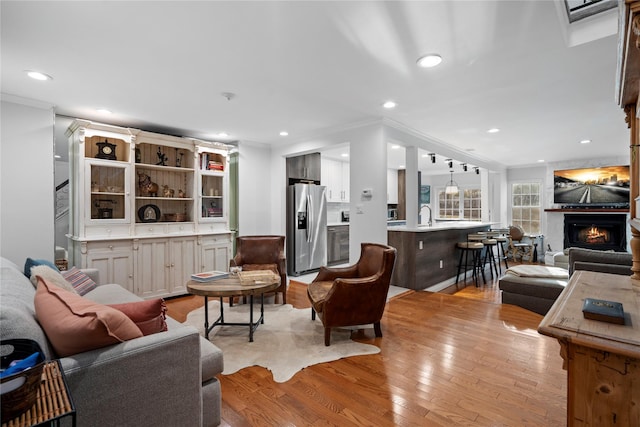 living room featuring a warm lit fireplace, light wood-style flooring, crown molding, and recessed lighting