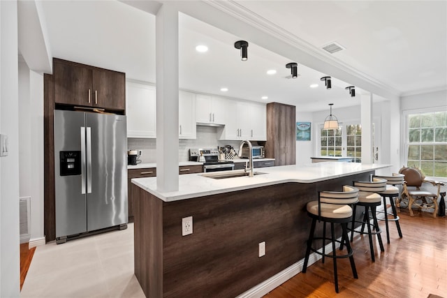 kitchen with stainless steel appliances, tasteful backsplash, visible vents, ornamental molding, and a sink