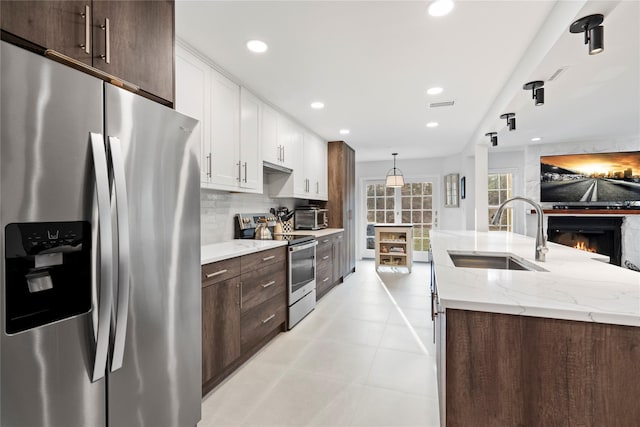 kitchen featuring dark brown cabinetry, decorative backsplash, stainless steel appliances, white cabinetry, and a sink