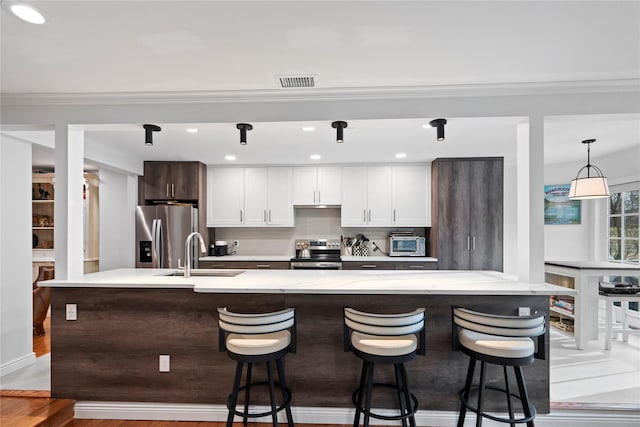 kitchen with visible vents, a breakfast bar area, appliances with stainless steel finishes, a sink, and backsplash