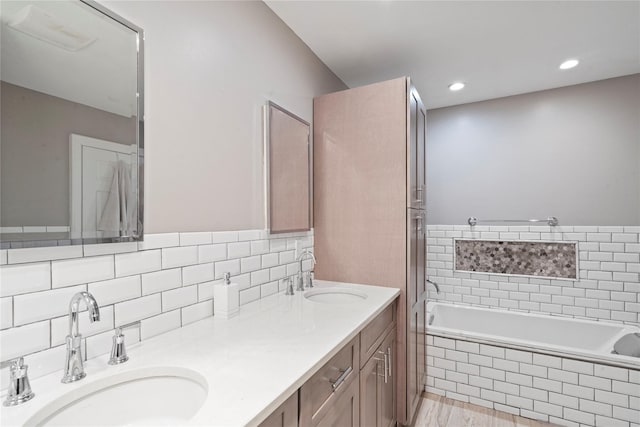 bathroom featuring double vanity, backsplash, a relaxing tiled tub, and a sink