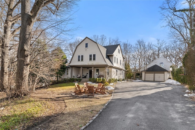 view of front facade with covered porch, a gambrel roof, a shingled roof, an outdoor structure, and a detached garage