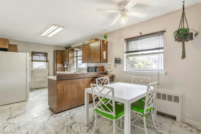 kitchen with marble finish floor, freestanding refrigerator, radiator, a peninsula, and brown cabinetry