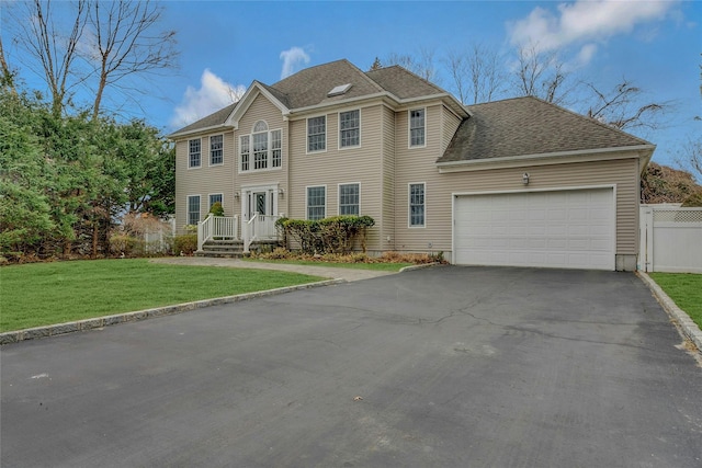 colonial home with a garage, aphalt driveway, roof with shingles, fence, and a front yard